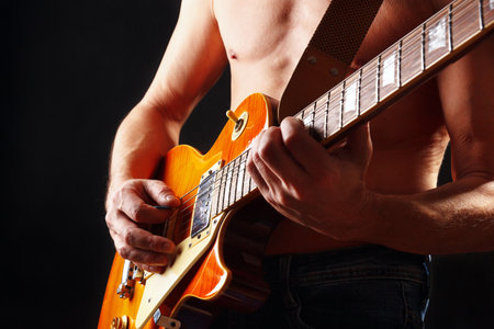 Rock musician plays the sunburst orange electric guitar on a dark stage.の写真素材