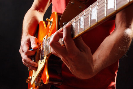 Musician in red plays the orange electric guitar on a dark stage.の写真素材