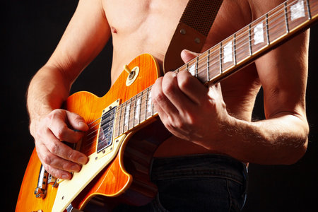 Musician with orange electric guitar on a dark stage.の写真素材