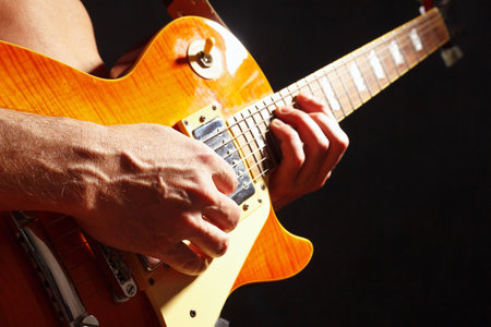Posing hands of musician playing the guitar on a dark stage.の写真素材