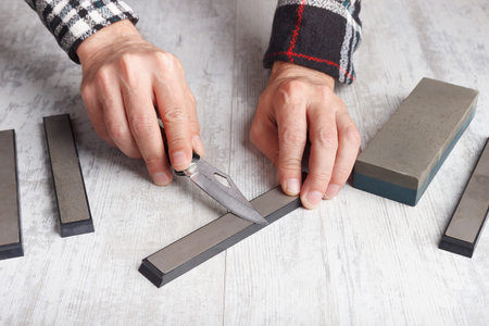 Sharpening small fishing on whetstone knife on a white table.