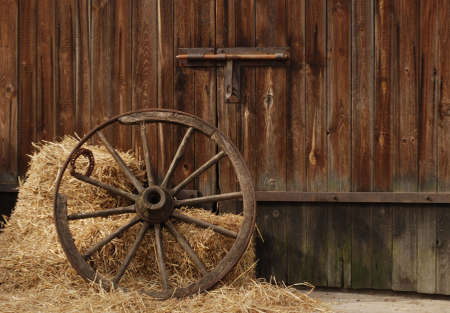 the old antique wheel from cart on background of hay and barnの写真素材