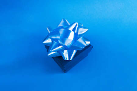 Closed blue gift box lies on the festive table. Monochrome holiday greeting card. New year, birthday, mother day or wedding present concept. Shiny bow lies on top of the present.の写真素材
