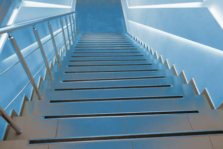 Modern classic stairs for descent down and rise up, illuminated by blue light. Dramatic background...