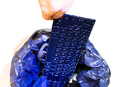 Male hand puts keyboard in office trash. Isolated garbage can, top view. Concept of electronic waste...