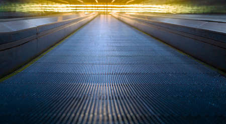 Modern metal escalator under bright yellow neon light. Concept of up motion. Part of airport terminal building and convenient escalatorの写真素材