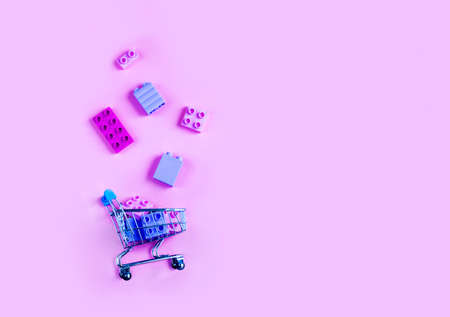 Toy shopping cart with children's constructor over pink background. Copy space for text or design. Monochrome concept of sale, discount and advertisement. Copy space for advertisement.の写真素材