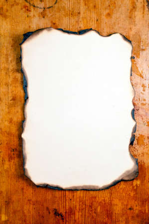 old yellowed sheet of burnt at the edges paper at wooden desk の写真素材