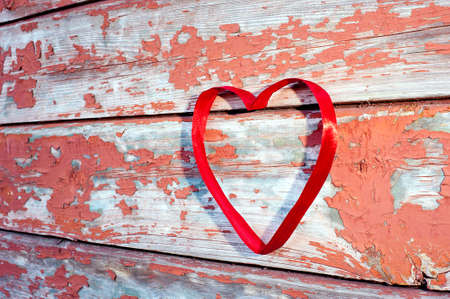 Red heart made of ribbon against old cracked boards - side view