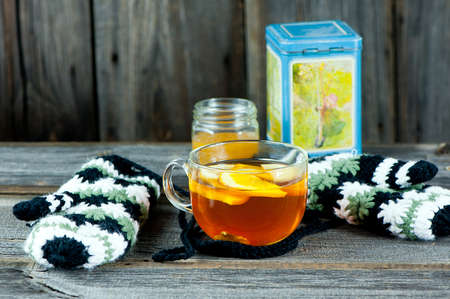 glass cup of warming ginger tea with slices of orange and lemon. Winter woolen gloves and tea...