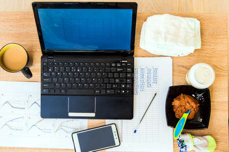 A concept image of having a baby and working at home. Organized workplace, diaper and porridge for a...