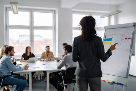 Rear view of businesswoman pointing at whiteboard during meeting in officeの素材