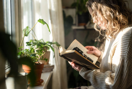 Young woman reading a book at home. Home interior with flowers.の素材