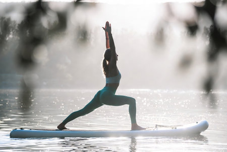 Young woman practicing yoga in the morning on a paddle board on the lakeの素材