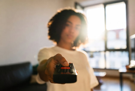 Young african american woman using remote control at home. Focus on handの素材