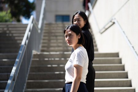 Two young Asian women walking down the stairs in a university campus.の素材