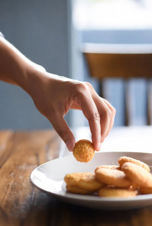 Close up of woman's hand holding fried nuggets on a plateの素材