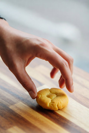 Woman's hand taking a cookie from a wooden table in the kitchenの素材