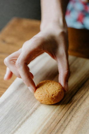 Woman's hands holding a cookie on a wooden cutting board. Selective focus.の素材
