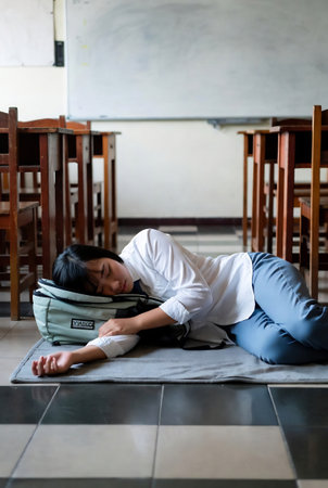 Young Asian woman student sleeping on the floor in classroom. Education concept.の素材