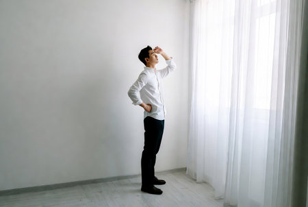 Businessman in white shirt and black pants standing near the window.の素材