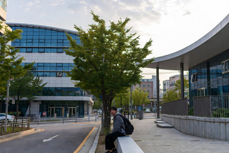 Man sitting on a bench in front of the modern office building.の素材
