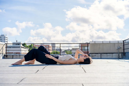 Young beautiful brunette woman in black pants and T-shirt posing on the roof of the buildingの素材