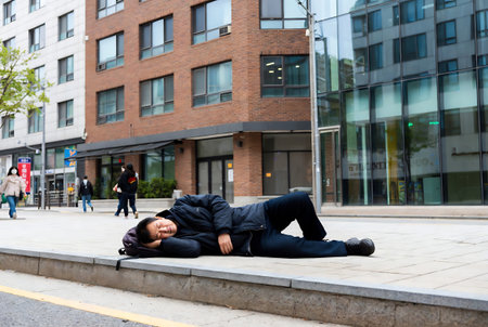 Young man sleeping on the street in front of a modern office buildingの素材