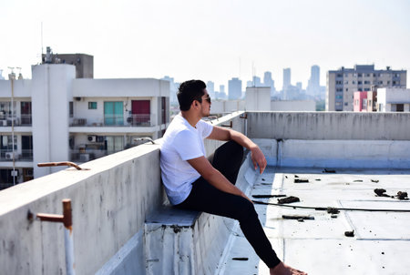 Young man sitting on the roof of a building and looking at the cityの素材