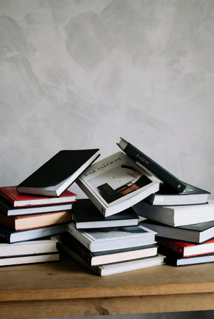 Pile of books on a wooden table against a gray wall.の素材