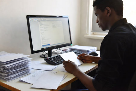 Young man working in office, he is using computer and writing notesの素材