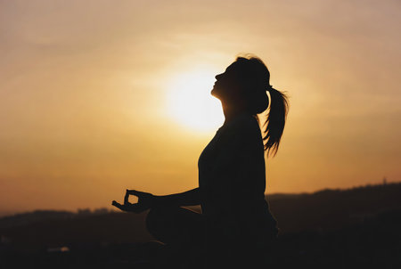 Silhouette of young woman practicing yoga on sunset background. Healthy lifestyle concept.の素材