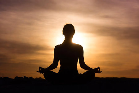 Silhouette of young woman practicing yoga in lotus position at sunsetの素材