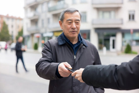 Asian senior man receiving money from his real estate agent at street.の素材