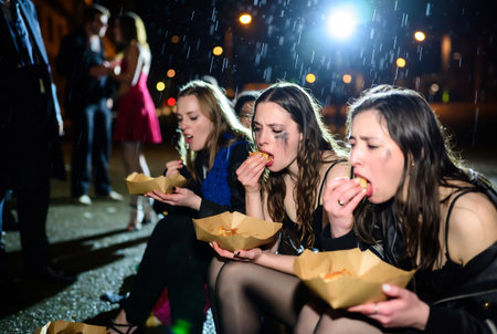Group of young friends eating fast food in the rain at night.の素材