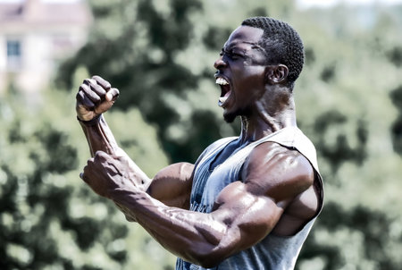 Healthy Young Man Standing Strong In The Park And Flexing Muscles - Muscular Athletic Bodybuilder Fitness Model Posing After Exercisesの素材