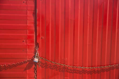 Rusty red metal door with old chain and locker. Metal fence background.