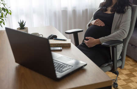 Pregnant woman is working on computer laptop and mobile phone, business. Being pregnant at work in office. Pregnant woman working on laptop at home.の写真素材
