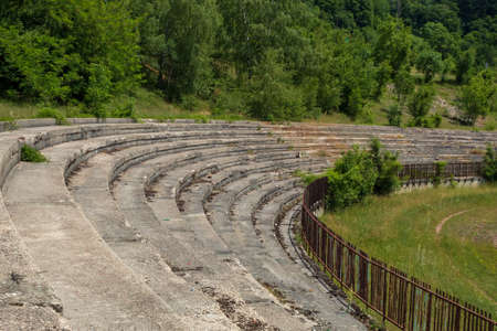 Abandoned concrete stands of the stadium, surrounded by a rusty fence. A bitten scene by the ravages of time.の写真素材