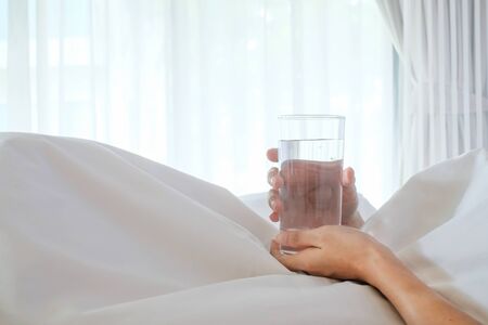 Asia woman holding glass of water on white bed with copy space for you design, morning concept.の写真素材