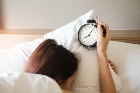 Woman sleep on the bed turns off the alarm clock wake up at the morning, Selective focus.の写真素材