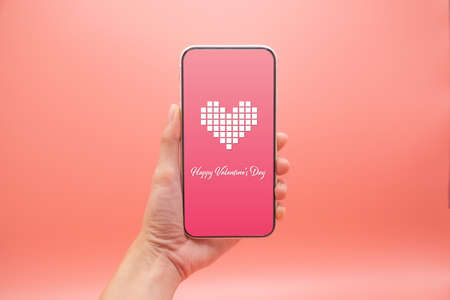 Women hand use smartphone with heart and valentine day screen on pink background, Valentine day concept.の写真素材