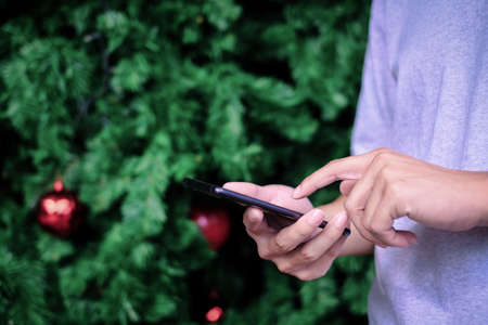 Man holding smartphone with christmas tree background, Technology concept.の写真素材