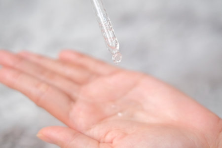 Woman hands apply cosmetic serum from bottle using pipette on carpet background, Health care concept.の写真素材
