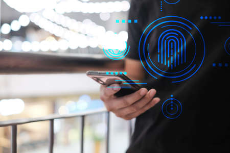 Closeup of male hand holding modern smartphone with fingerprint icon, man's hand using cellphone at night city, bokeh light, Selective focus.の写真素材