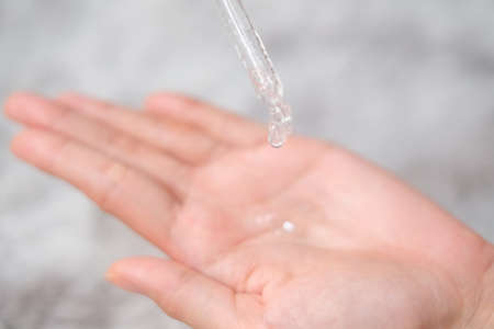 Woman hands apply cosmetic serum from bottle using pipette on carpet background, Health care concept.の写真素材