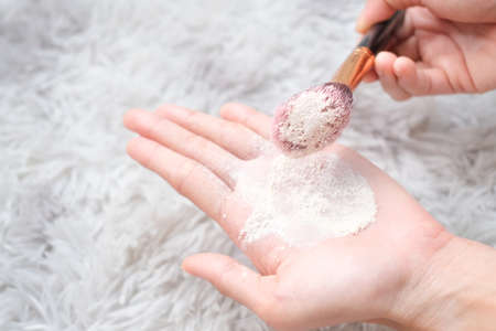 Close up woman holding talc make up and brush on carpet background, beauty concept.