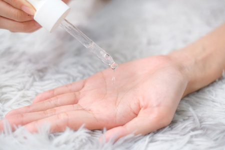 Woman hands apply cosmetic serum from bottle using pipette on carpet background, Health care concept.の写真素材