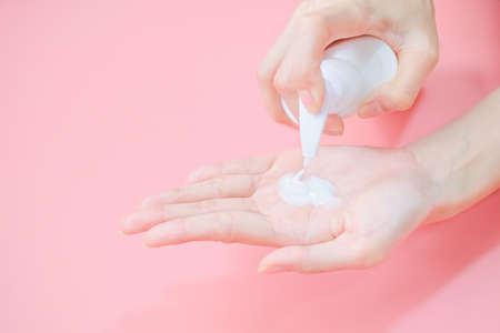 Woman applying moisturizing hand cream on hand with pink background, Health care concept.の写真素材