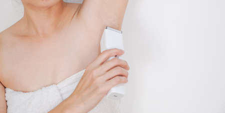 Woman shaving armpit with clipper on white background.